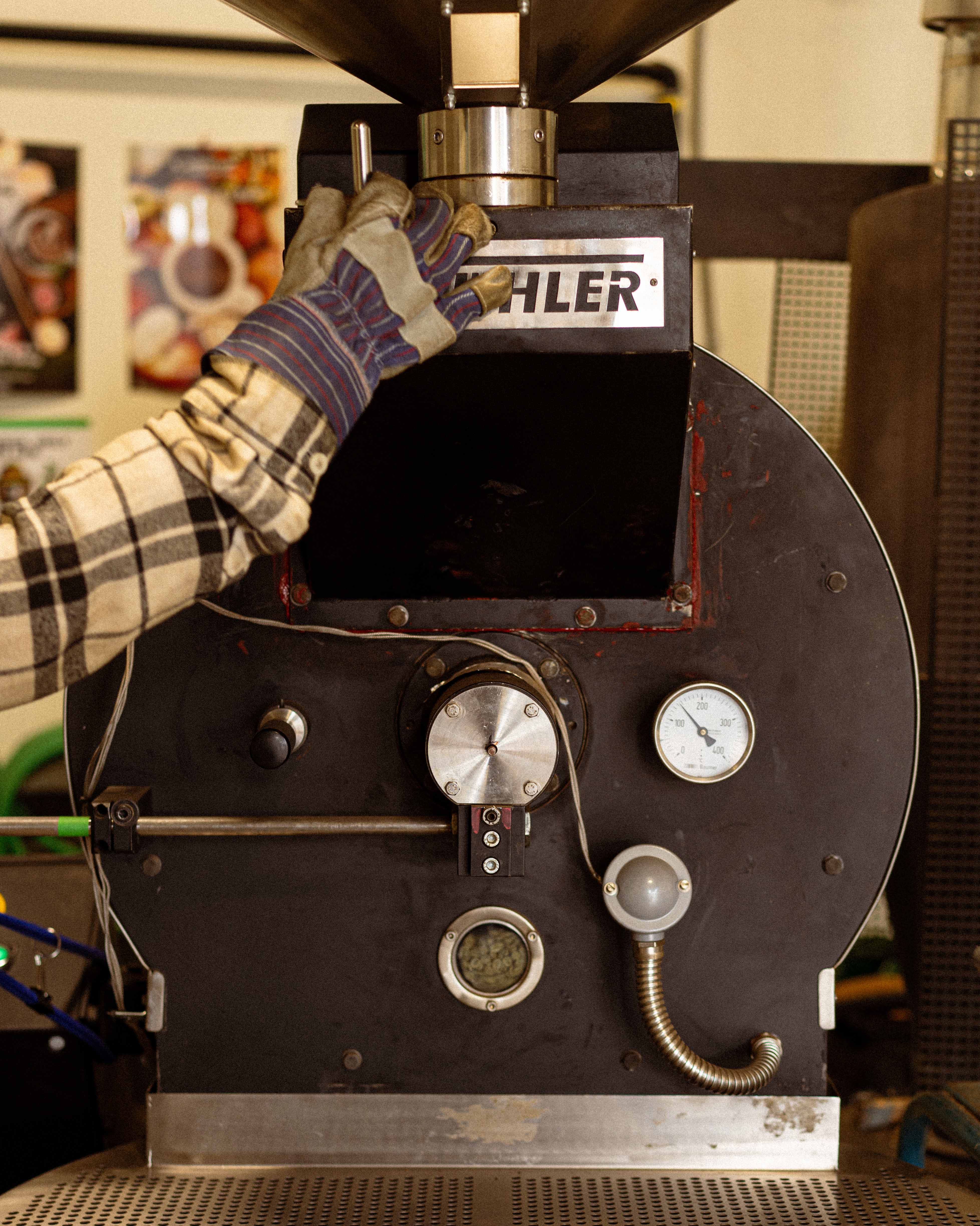 Person wearing gloves operating a coffee roaster with 'Buhler' branding.