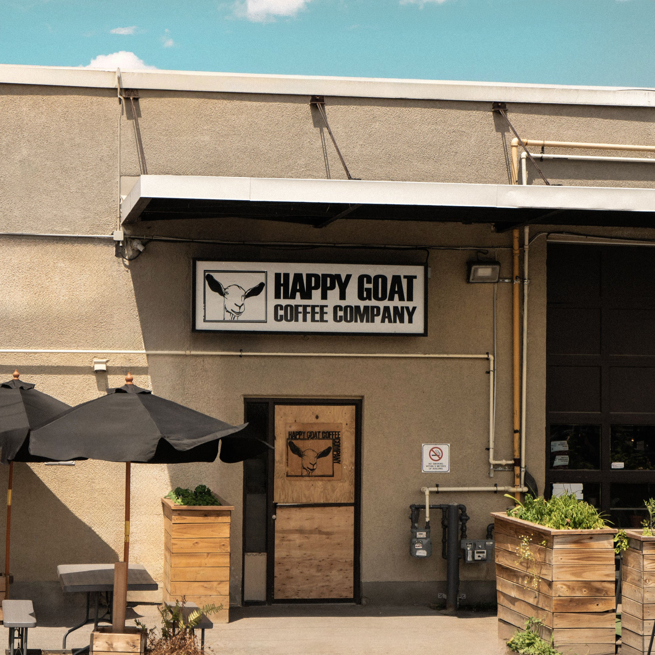 Happy Goat Coffee Company building exterior with sign and outdoor seating area.
