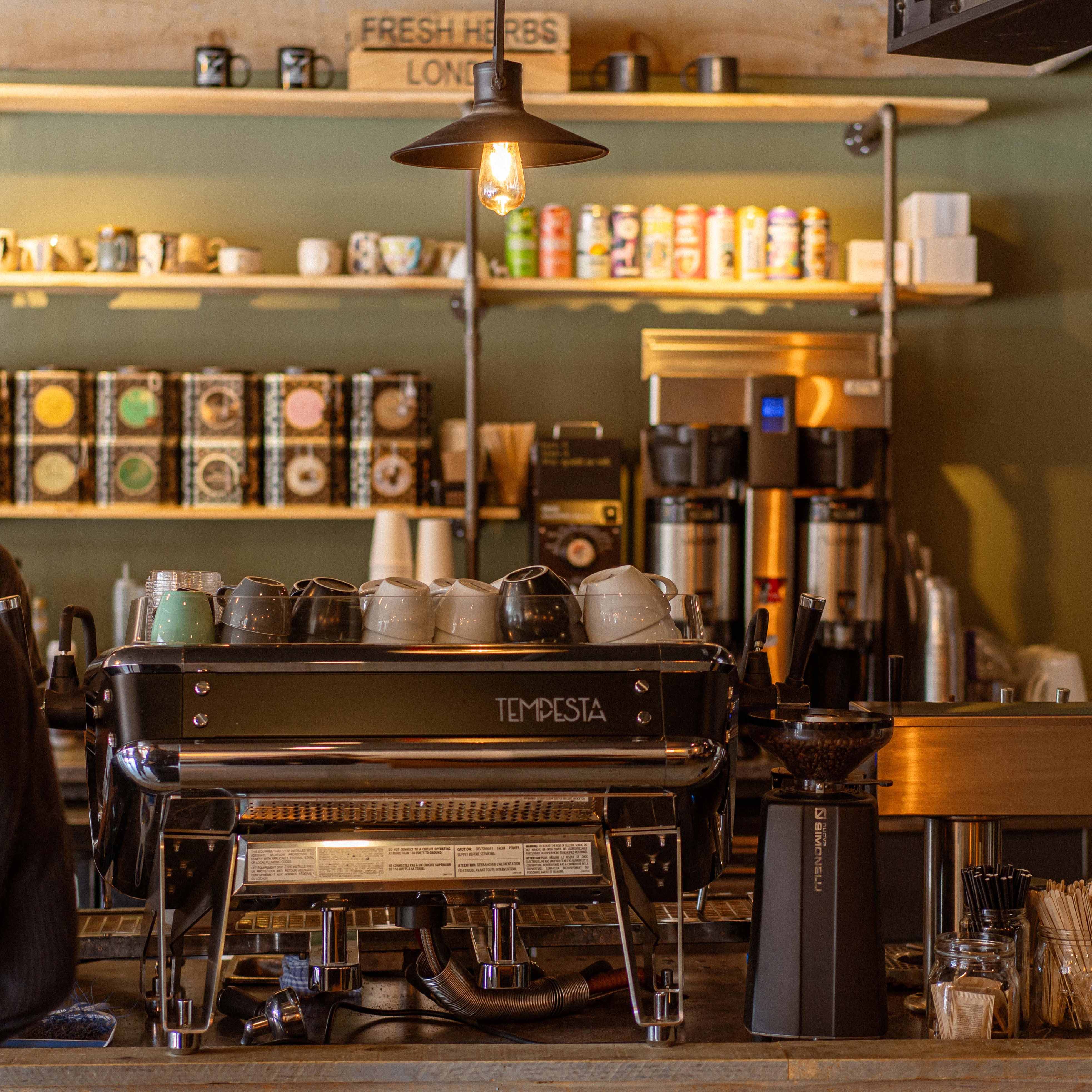 Coffee shop counter with coffee-making equipment and shelves displaying coffee beans and cups.